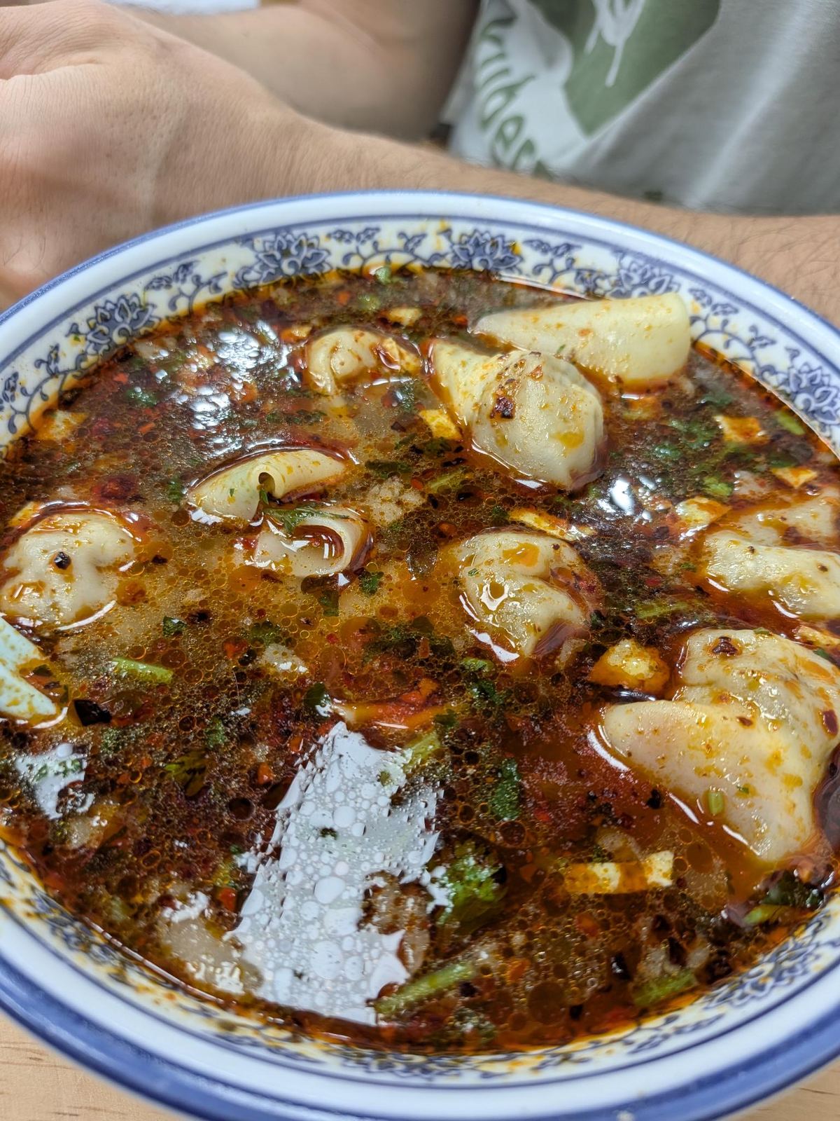 Bol épicé à l'huile de piment, wontons flottants et herbes vertes, bol bleu et blanc
