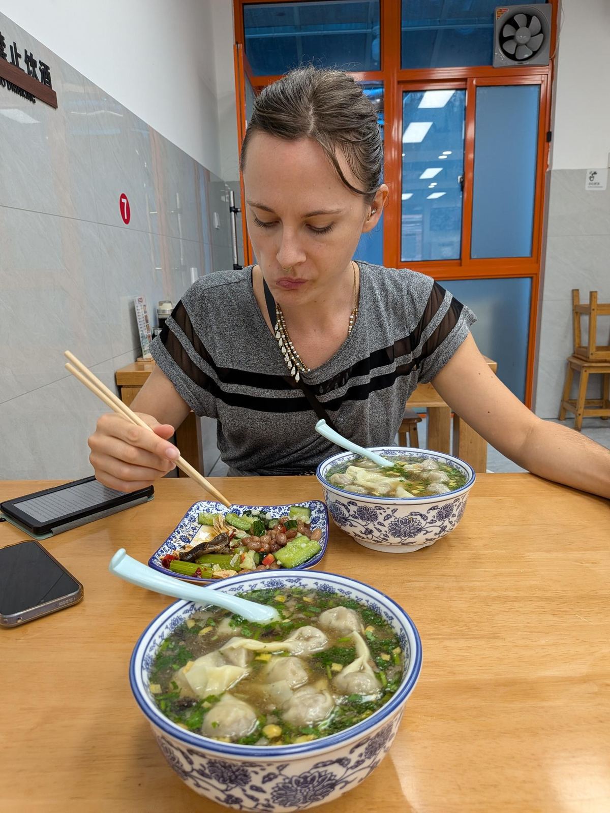 Marion devant ses deux bols de wontons, assiette de légumes marinés et cacahuètes à côté, signe 禁止饮酒 au mur