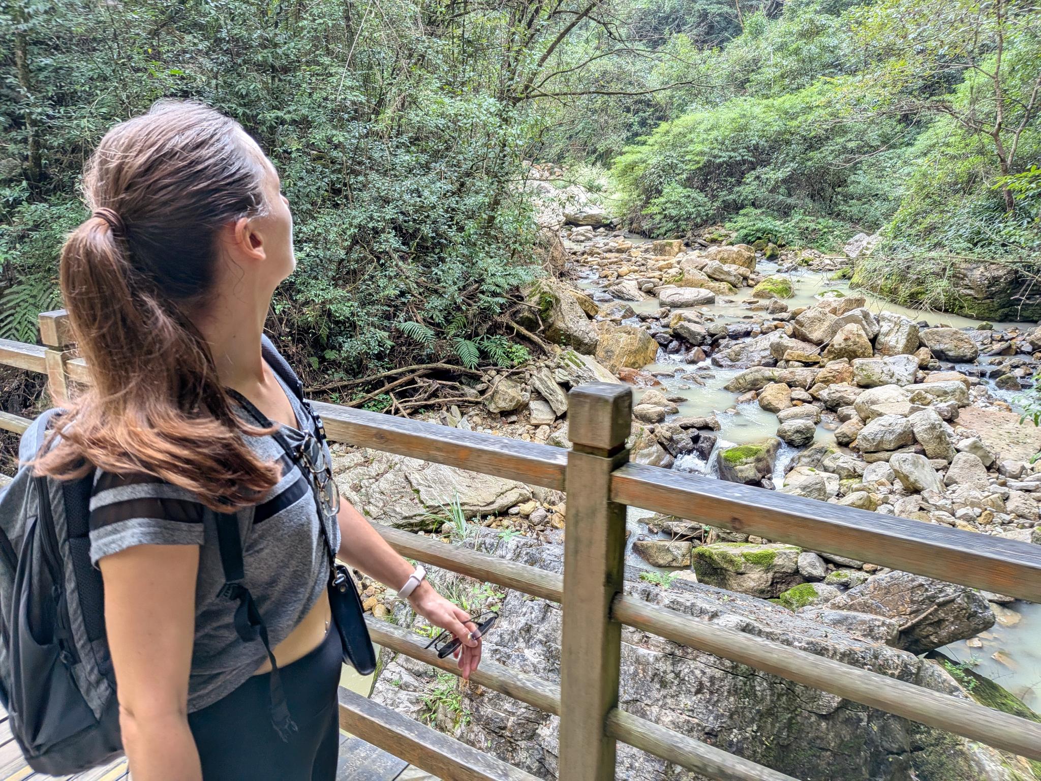 Marion au garde-fou en bois, la rivière boueuse et ses cascades sur les rochers