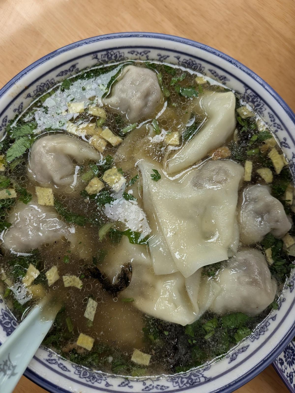 Wontons en bouillon clair vu de dessus, coriandre et croûtons, bol blanc à liseré bleu fleuri