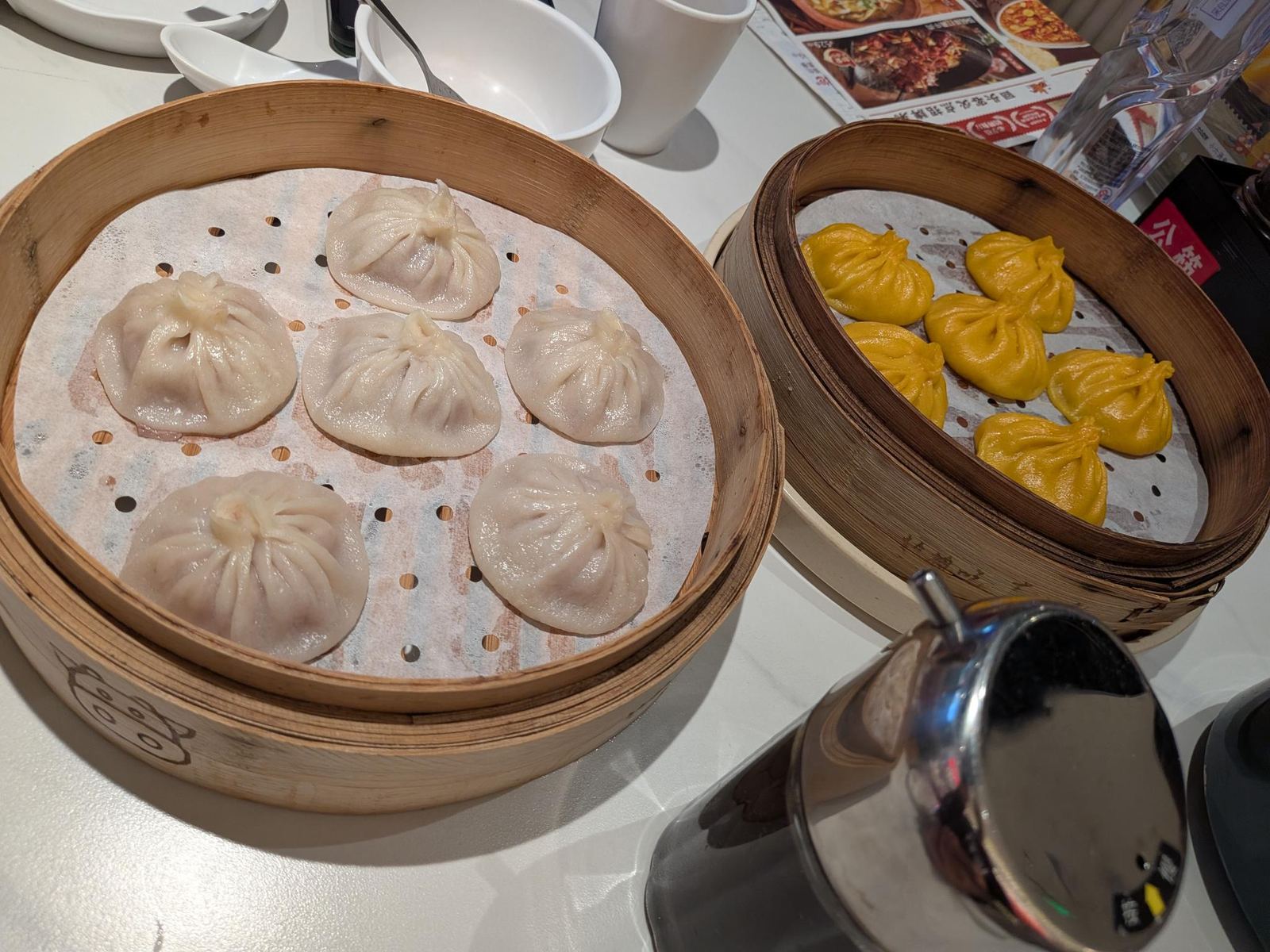 Deux paniers vapeur : des xiaolongbao clairs et de petites boulettes jaunes, sur la table du restaurant du mall