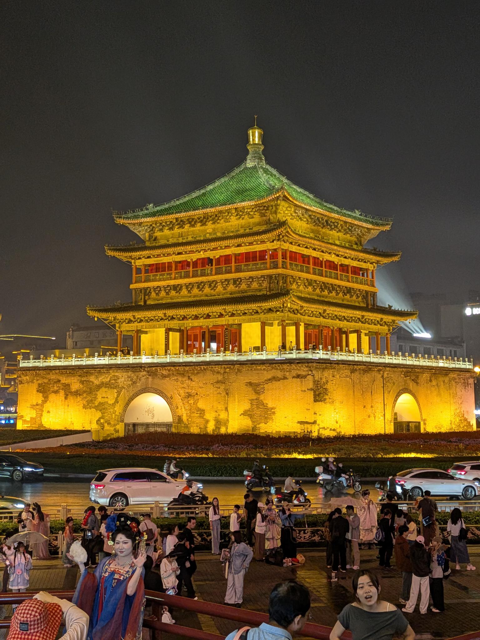 La Cloche de Xi'an illuminée d'or à la nuit, foule de touristes en hanfu sur la place mouillée
