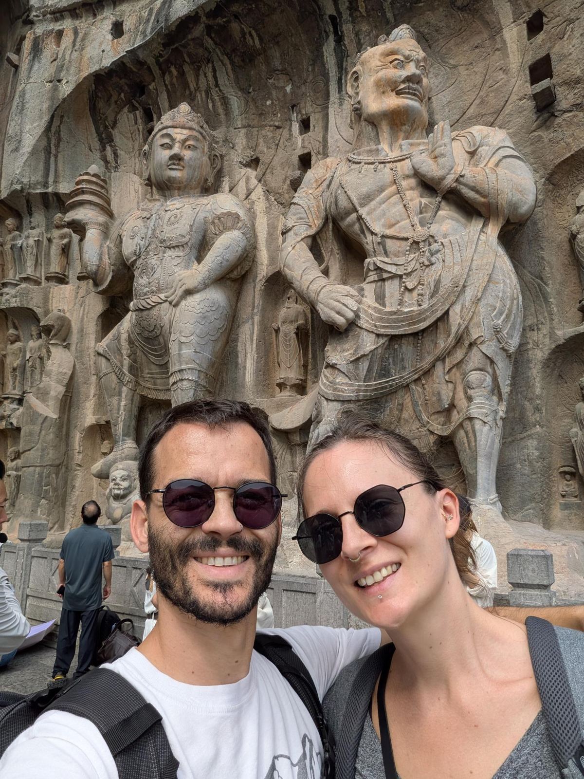 Selfie du couple devant les deux gardiens de pierre sculptés dans la falaise, visiteurs sur la plateforme en contrebas