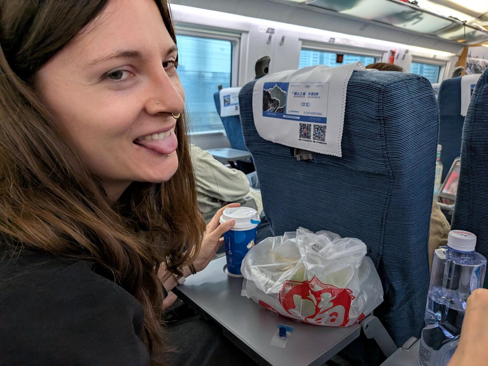 Marion dans le wagon du train, son café à la main, langue tirée pour la route