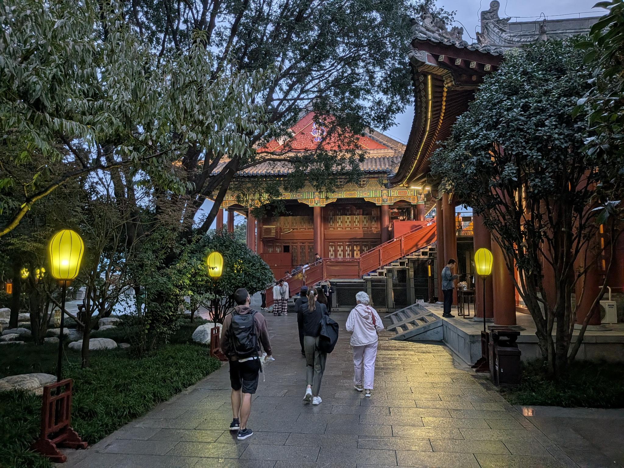 Salle rouge laquée à deux niveaux au crépuscule, escalier rouge, lanternes jaunes dans la cour