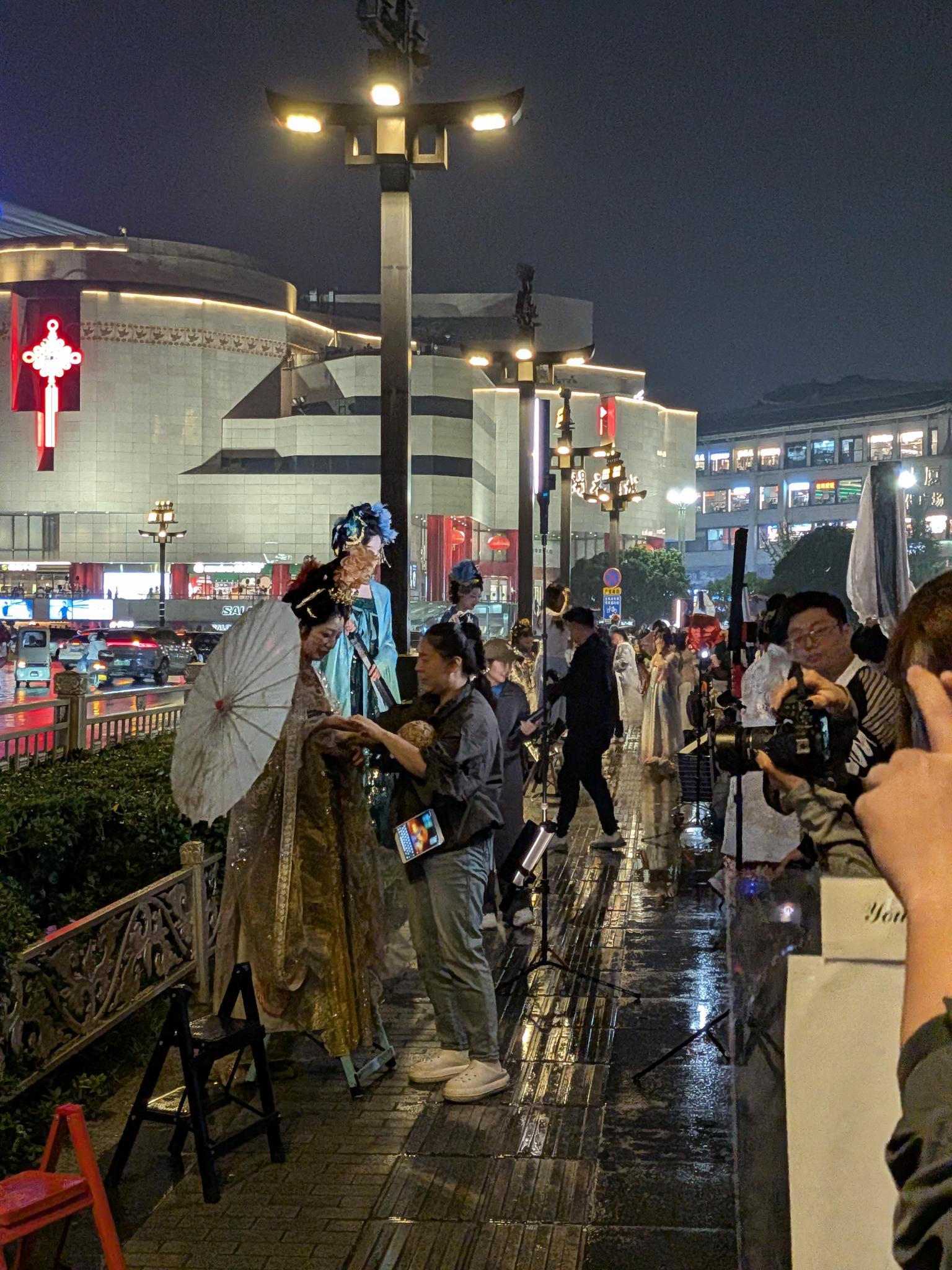 Modèle en hanfu à l'éventail, photographe au DSLR devant l'immeuble au nœud chinois rouge lumineux