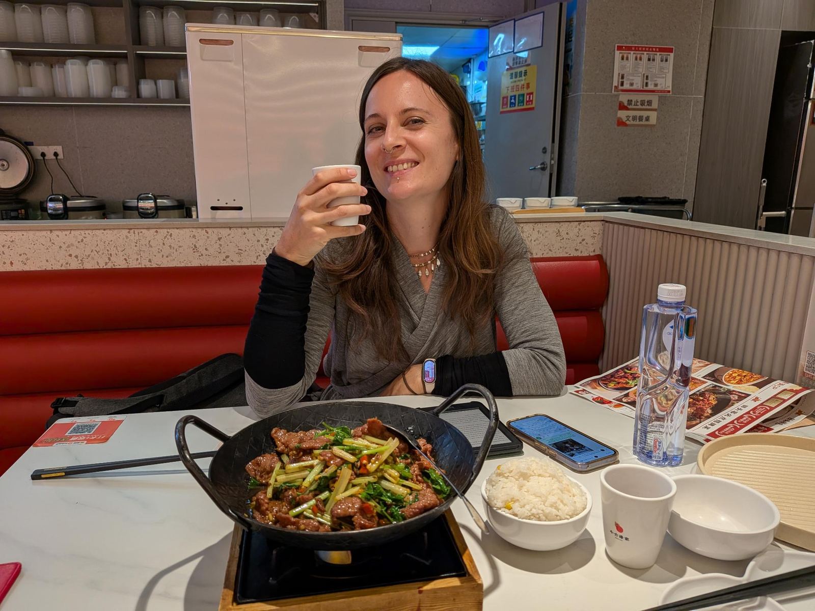 Marion qui lève son petit verre vers la caméra, wok de bœuf sauté sur son support en bois au feu, bol de riz sur la table