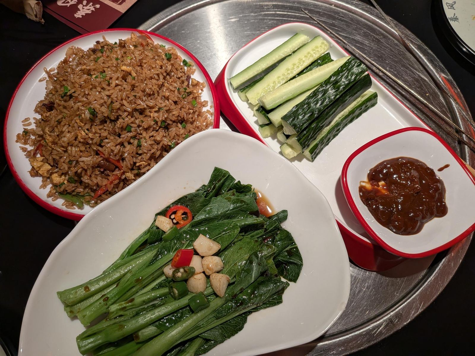 Plateau de barbecue : riz saumé au piment, bâtons de concombre, feuilles blanchies à l'ail, sauce brun foncé, brochettes posées sur le plateau métallique