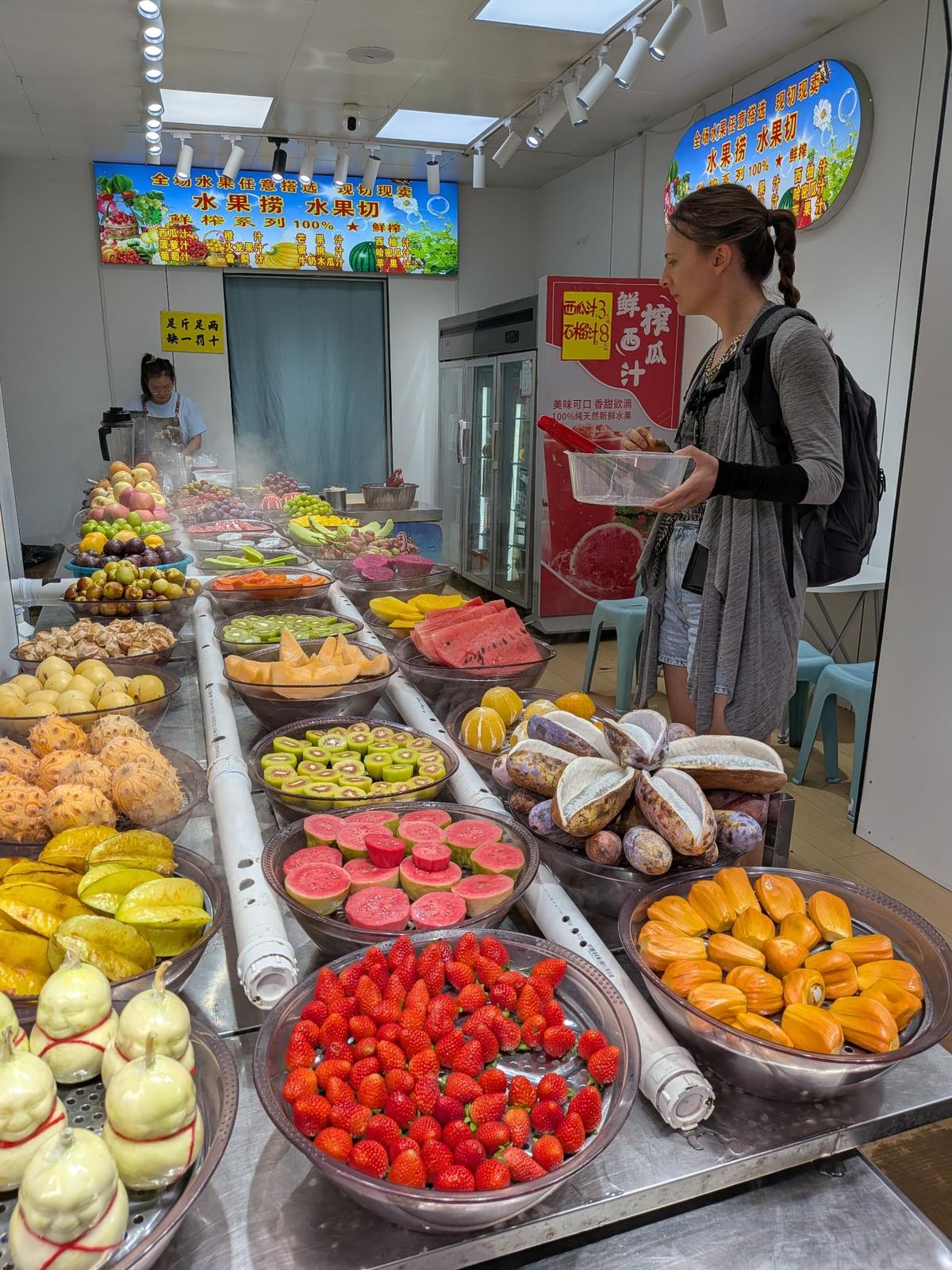 Comptoir de fruits coupés : fraises, kumquats, kiwis, pastèques, mangues, pamplemousses, pancarte 水果捞 100% 鲜榨 et prix 西瓜汁 3元 石榴汁 8元
