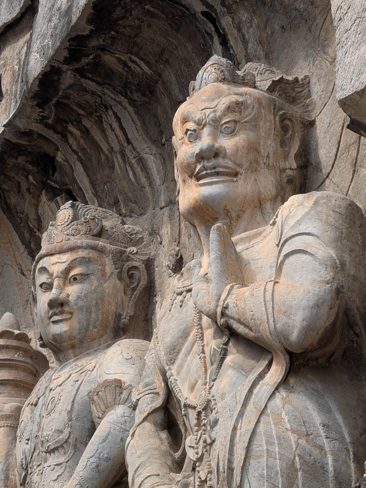 Deux gardiens de pierre gravés dans la falaise, l'un au visage féroce et mains jointes, l'autre plus posé, petites stoupas au bas de la paroi