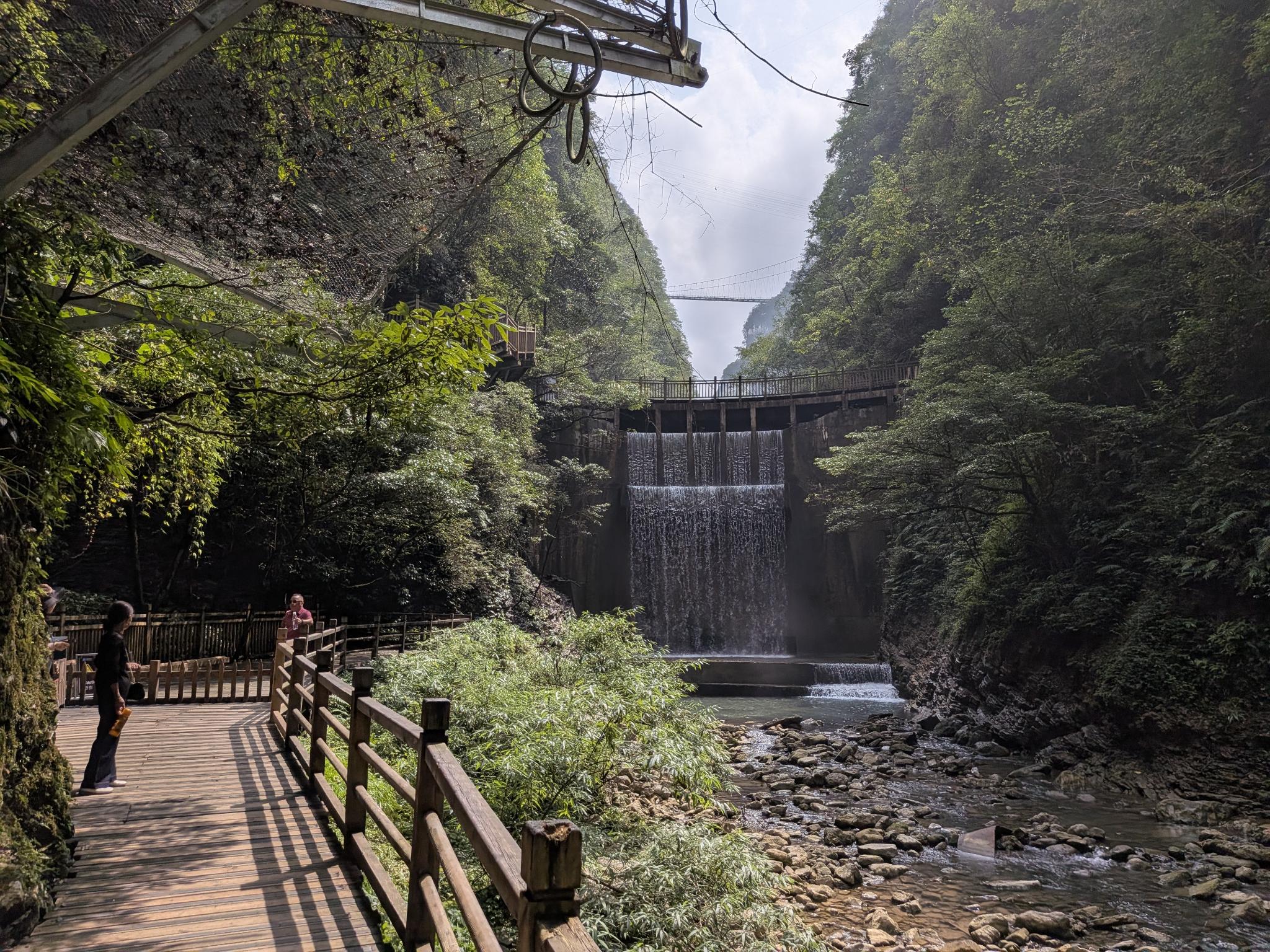 Le petit barrage en cascade et le pont suspendu au fond de la vallée
