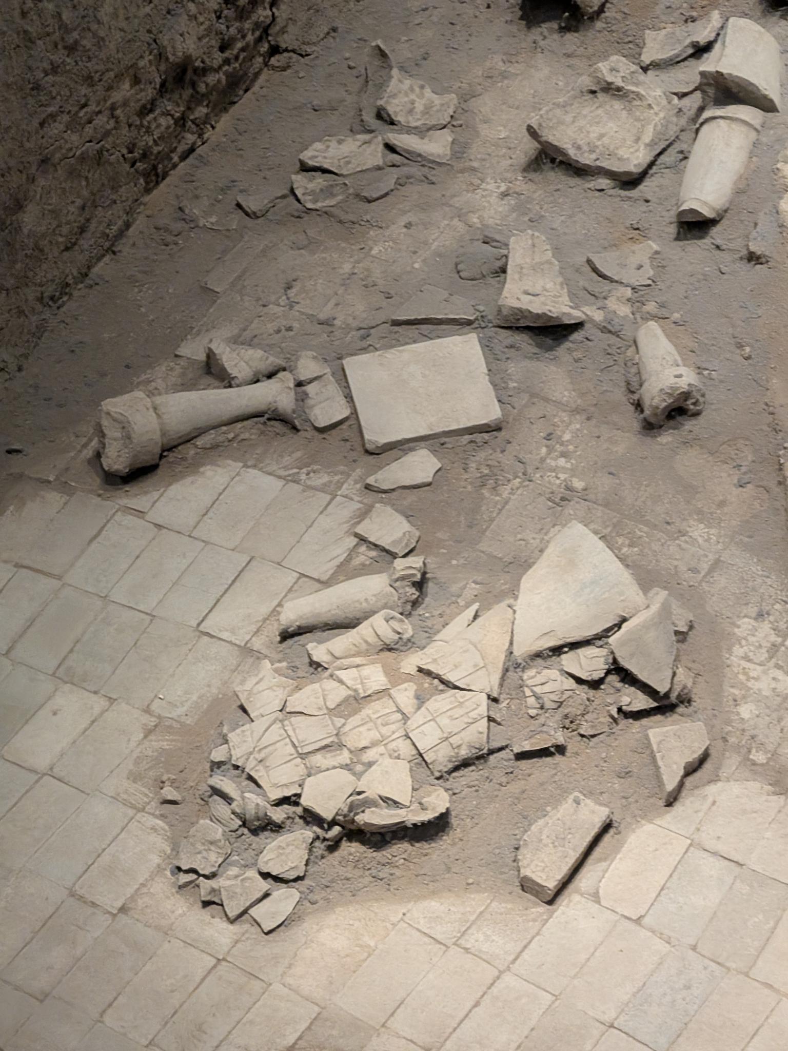 Sol pavé en tuiles partiellement intact avec fragments et colonnes de pierre cassées au sol