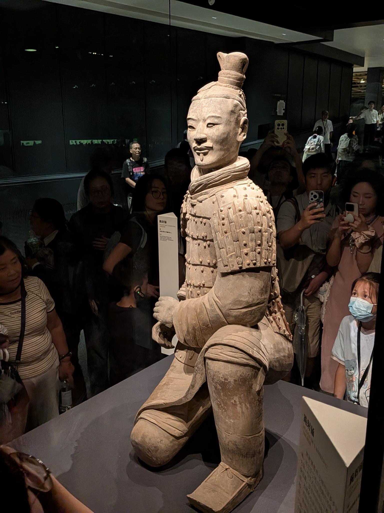 L'archer à genoux (跪射俑) derrière sa vitrine, foule au smartphone et pancarte KNEELING ARCHER