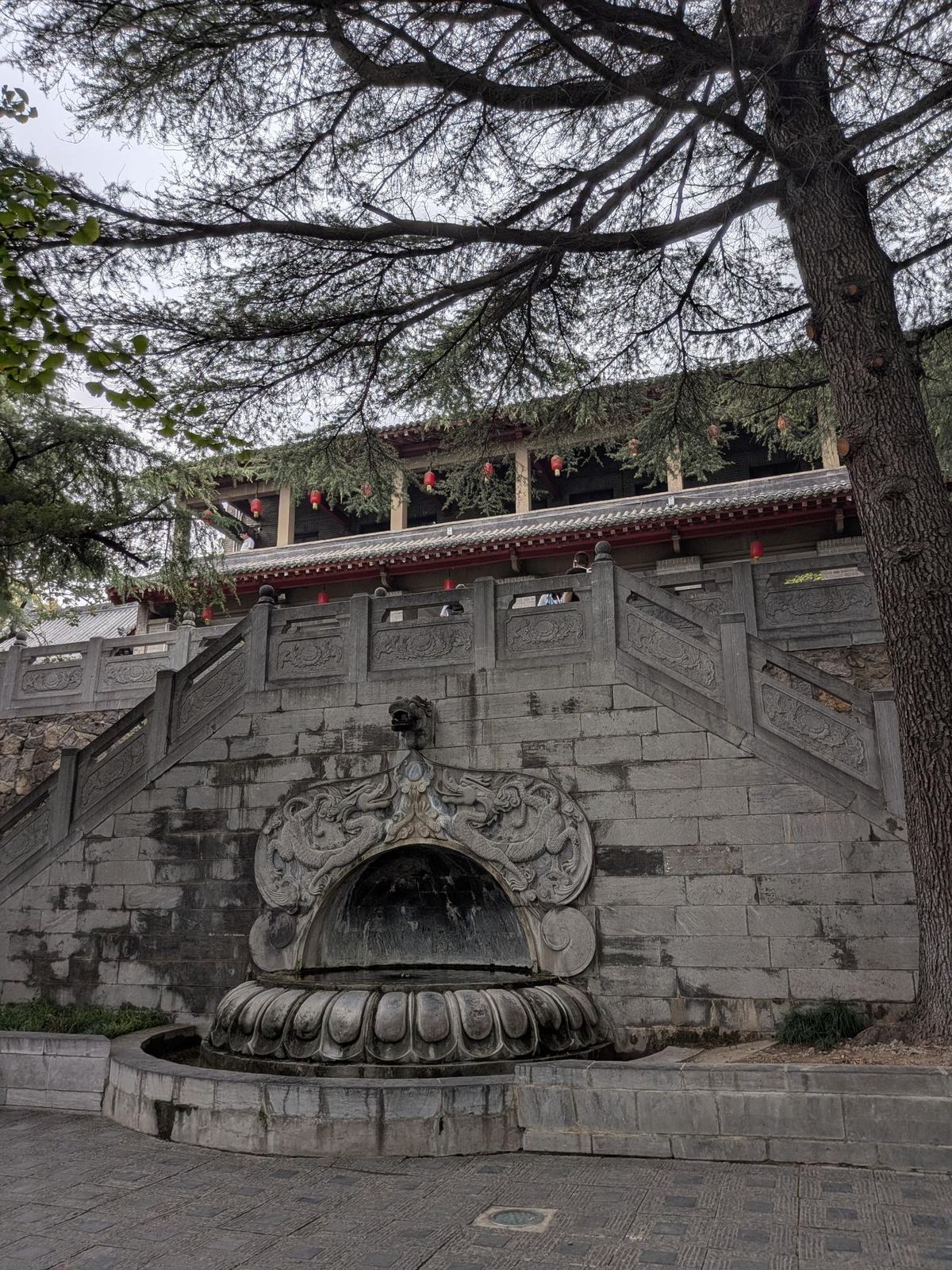 La fontaine de pierre du temple, bassin à pétales de lotus sculptés, dosseret aux dragons, mur en terrasse et bâtiment à colonnes rouges avec lanternes