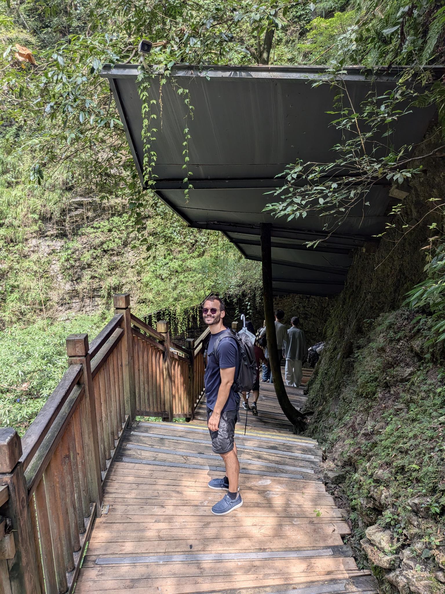 Tristan souriant sous la passerelle couverte, les lianes et son dôme de métal