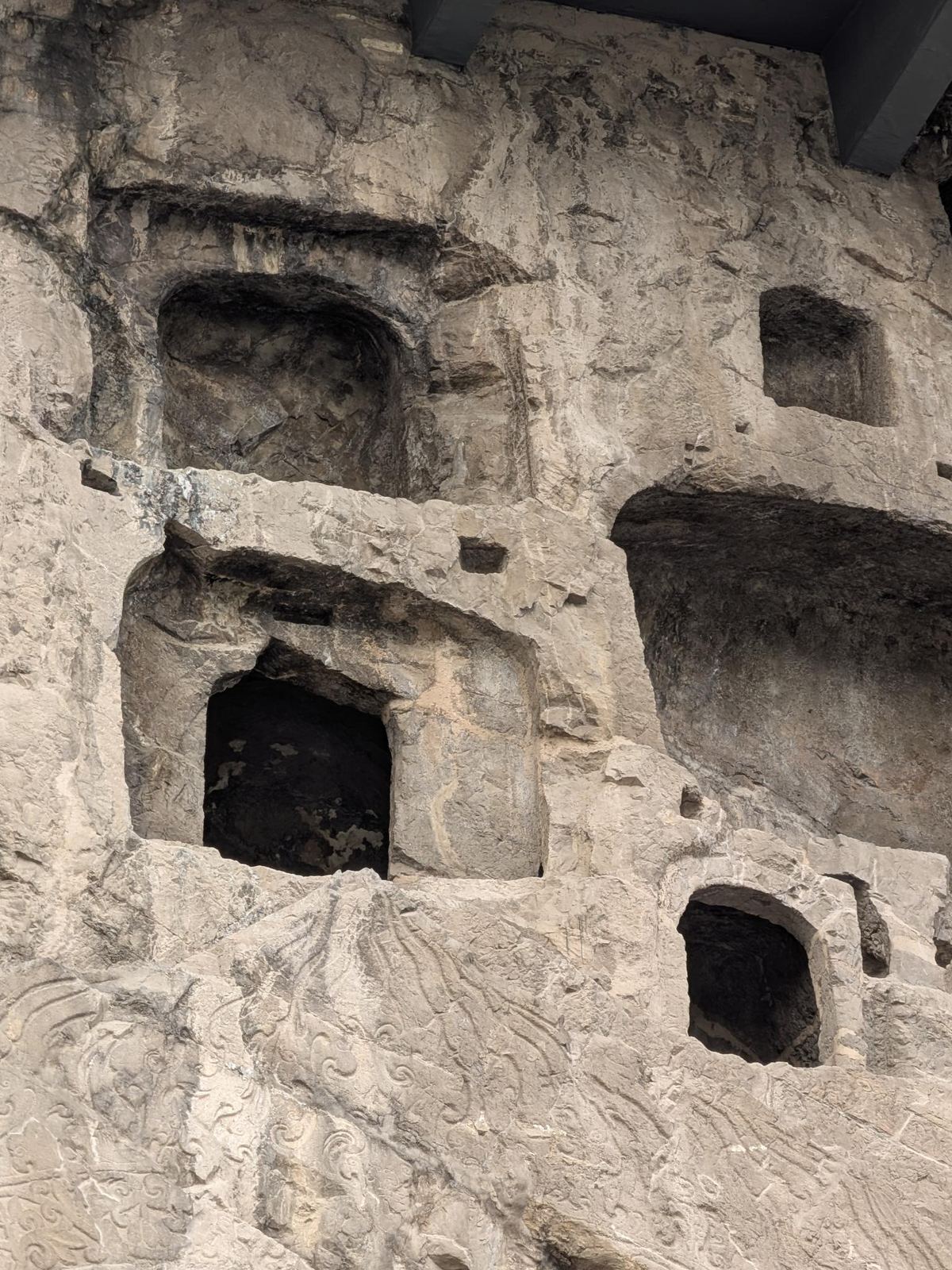 Falaise érodée couverte de niches et de cavités de formes irrégulières, bas-reliefs de nuages et de vagues dans la partie basse, toit de protection au sommet