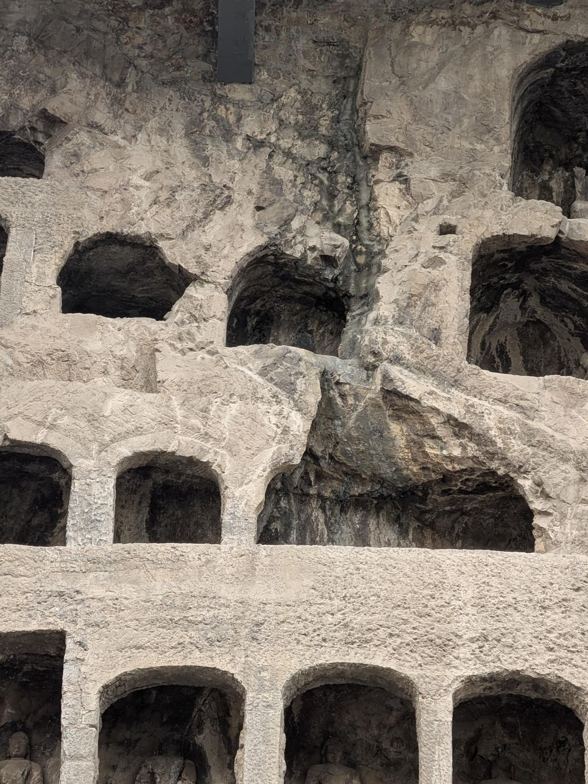 Rangées de niches en arche dans la falaise, section centrale effondrée, Bouddhas assis dans la rangée du bas et cavités vides en haut