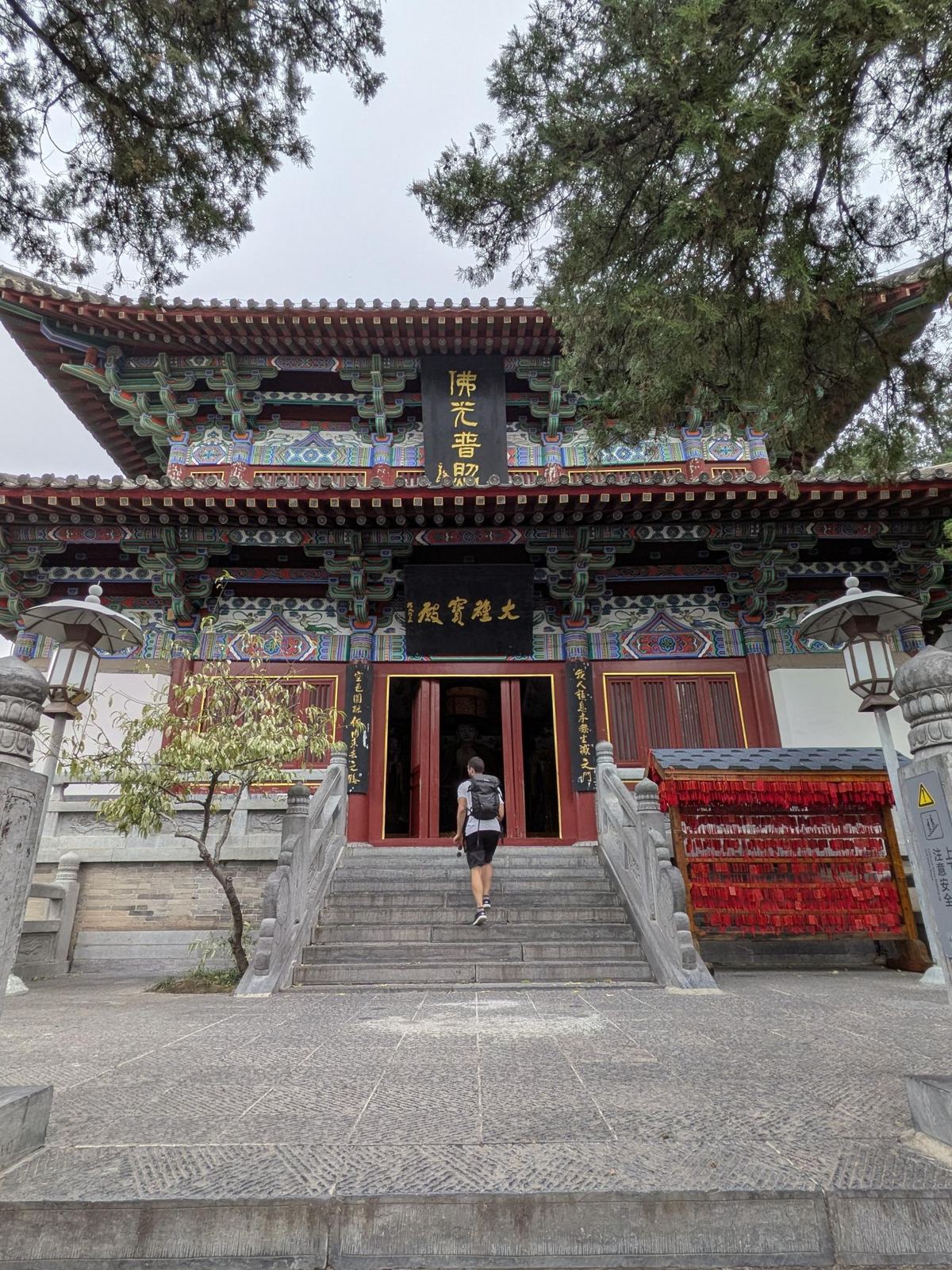 L'entrée du grand hall du temple, colonnes rouges et encorbellements peints, tablettes 佛光普照 et 大雄宝殿, étal de banderoles rouges de vœux à droite