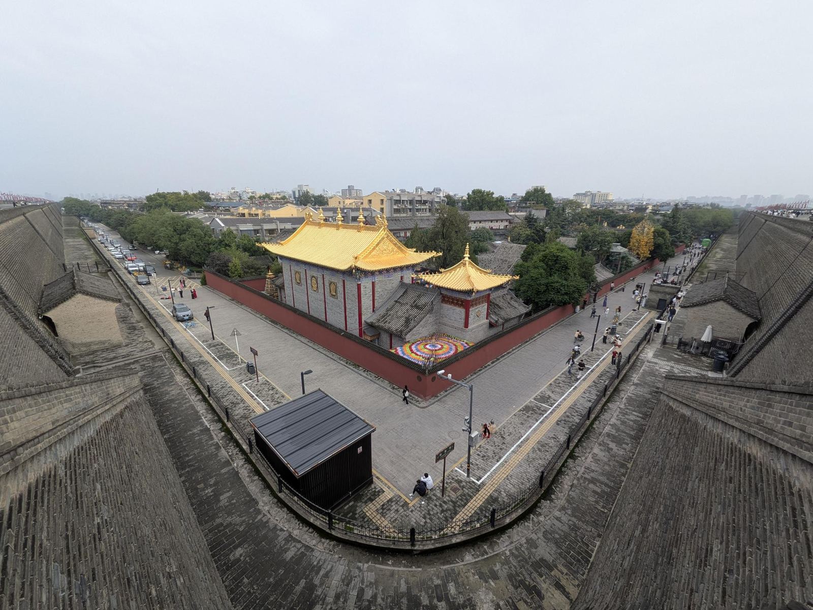 Vue depuis le rempart sur une place avec temple aux toits dorés, mandala coloré dans la cour, immeubles en arrière-plan