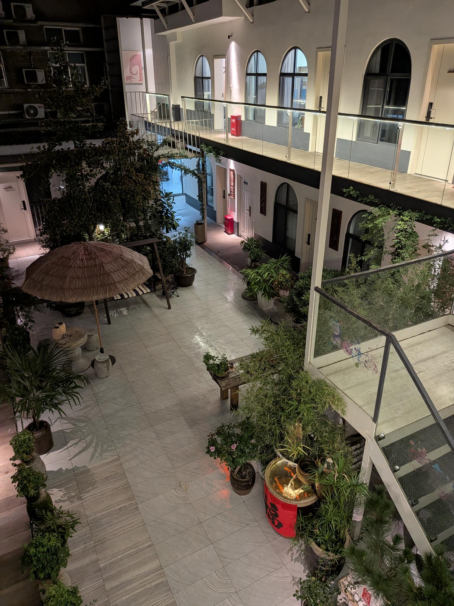 La cour de l'hôtel Yin Li Bei Yuan : plantes, parasol de paille, bassin à carpes koï, banderole 福