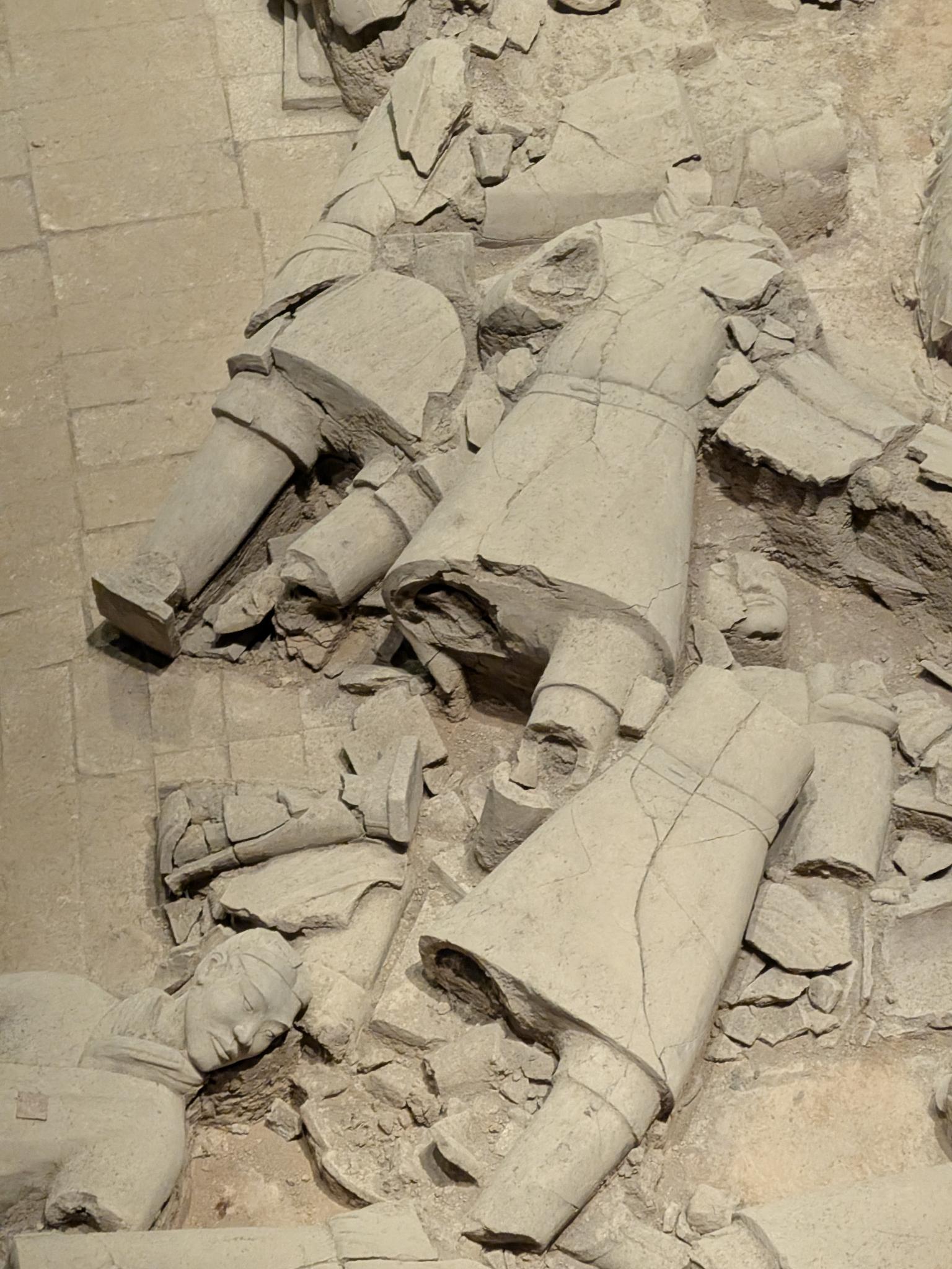 Fragments de statues cassées éparpillés au sol de la tranchée, deux têtes intactes au milieu des débris
