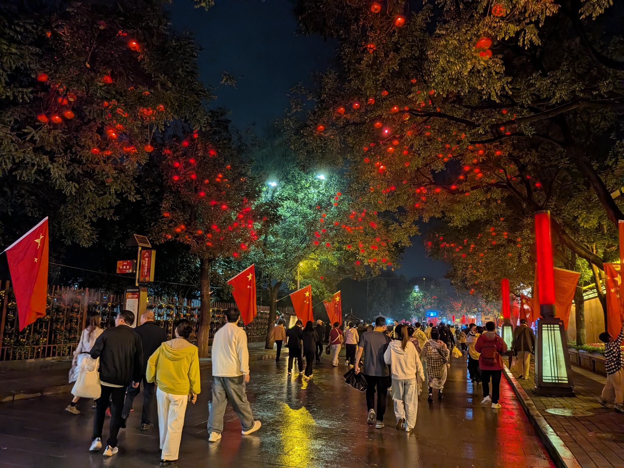 Rue piétonne de nuit avec lanternes rouges et drapeaux nationaux, pavé mouillé, lampadaires rouges et enseignes de jardins de cour