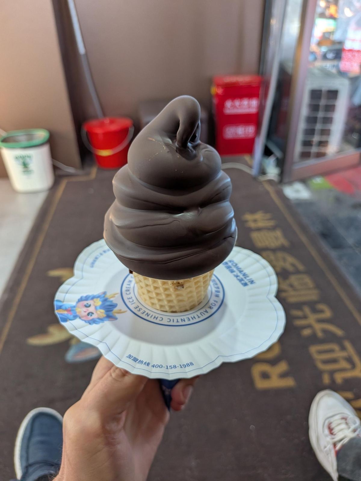 Le soft-serve chocolat de la maison ROMANLIN dans son cornet gaufre, sur son socle papier FOR AUTHENTIC CHINESE ICE CREAM