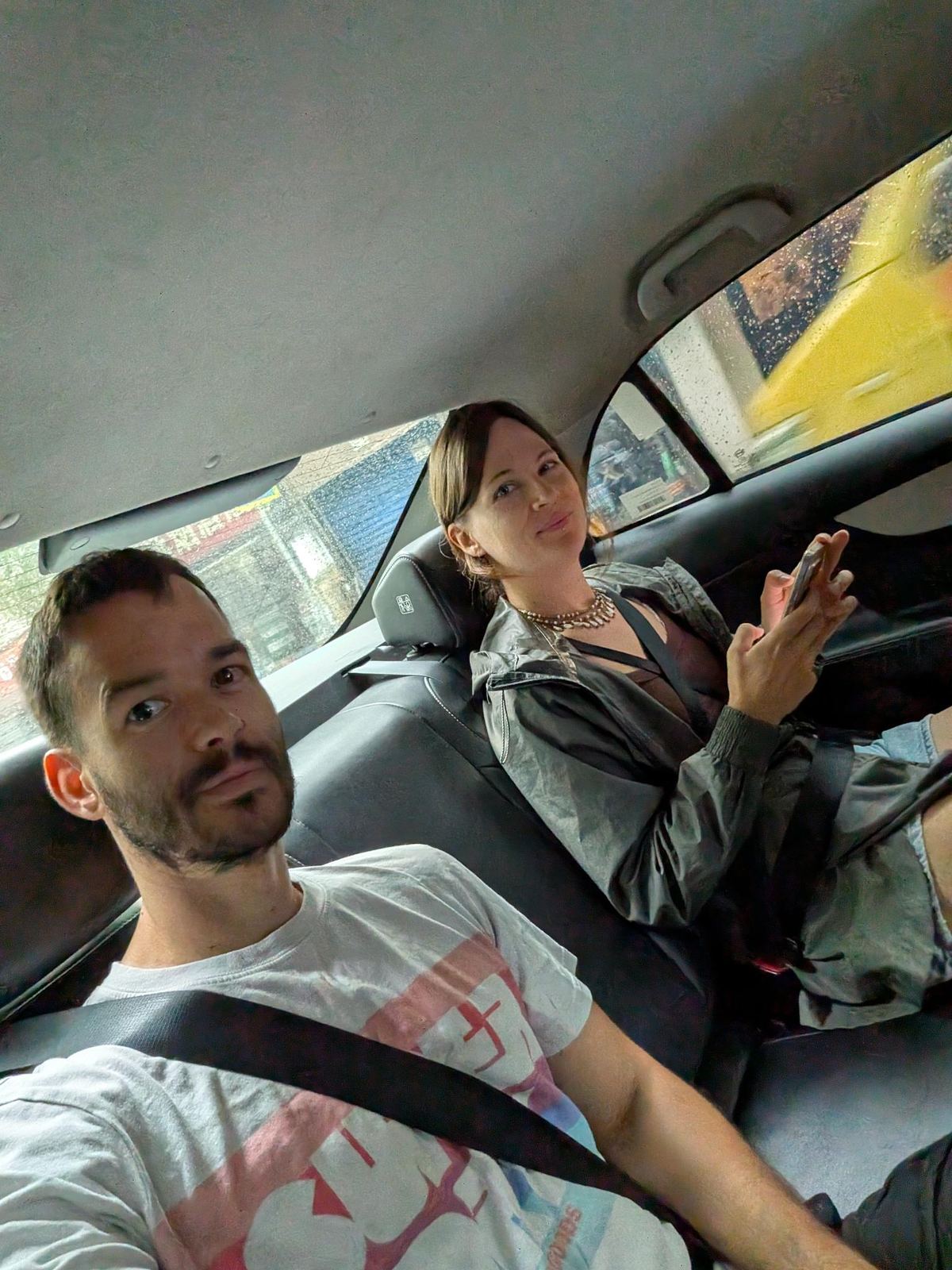 Selfie dans le taxi sous la pluie, Tristan à l'avant et Marion au smartphone à l'arrière
