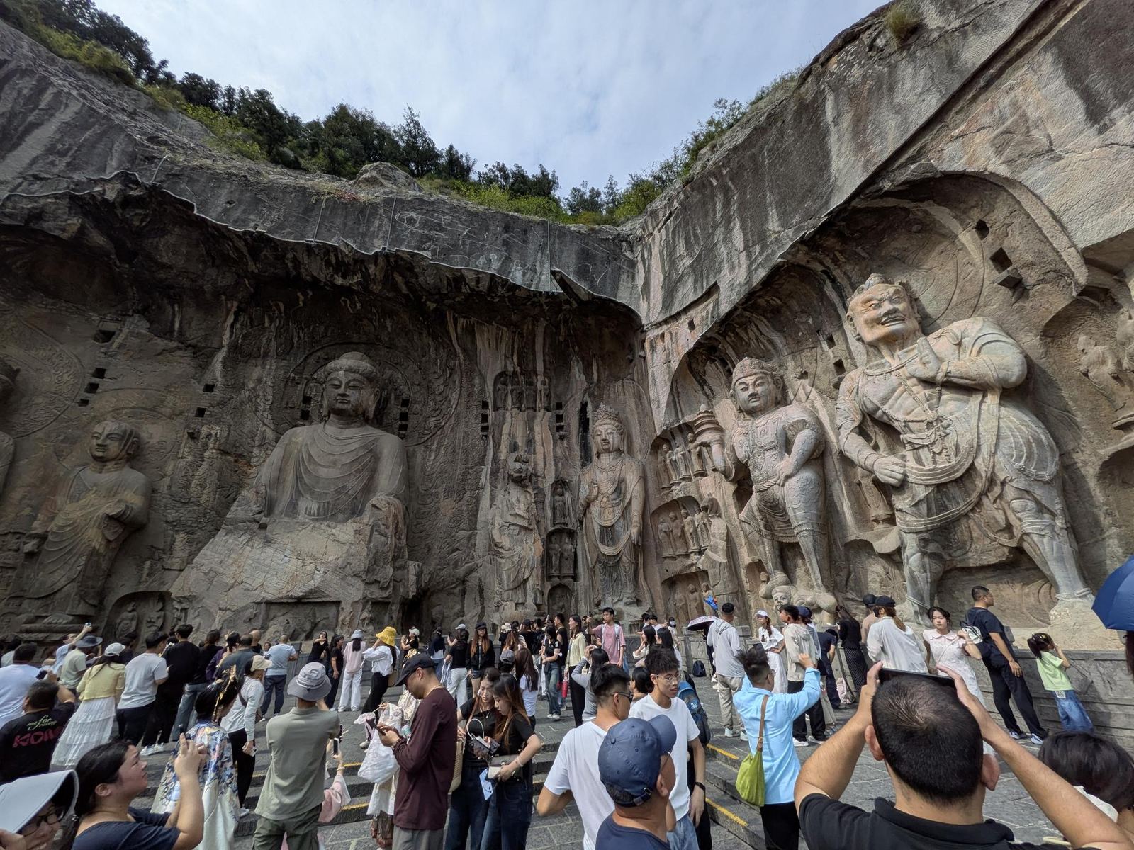 Le Bouddha géant de Fengxian dans sa niche, entouré de ses figures de cour debout, foule de smartphones levés en premier plan