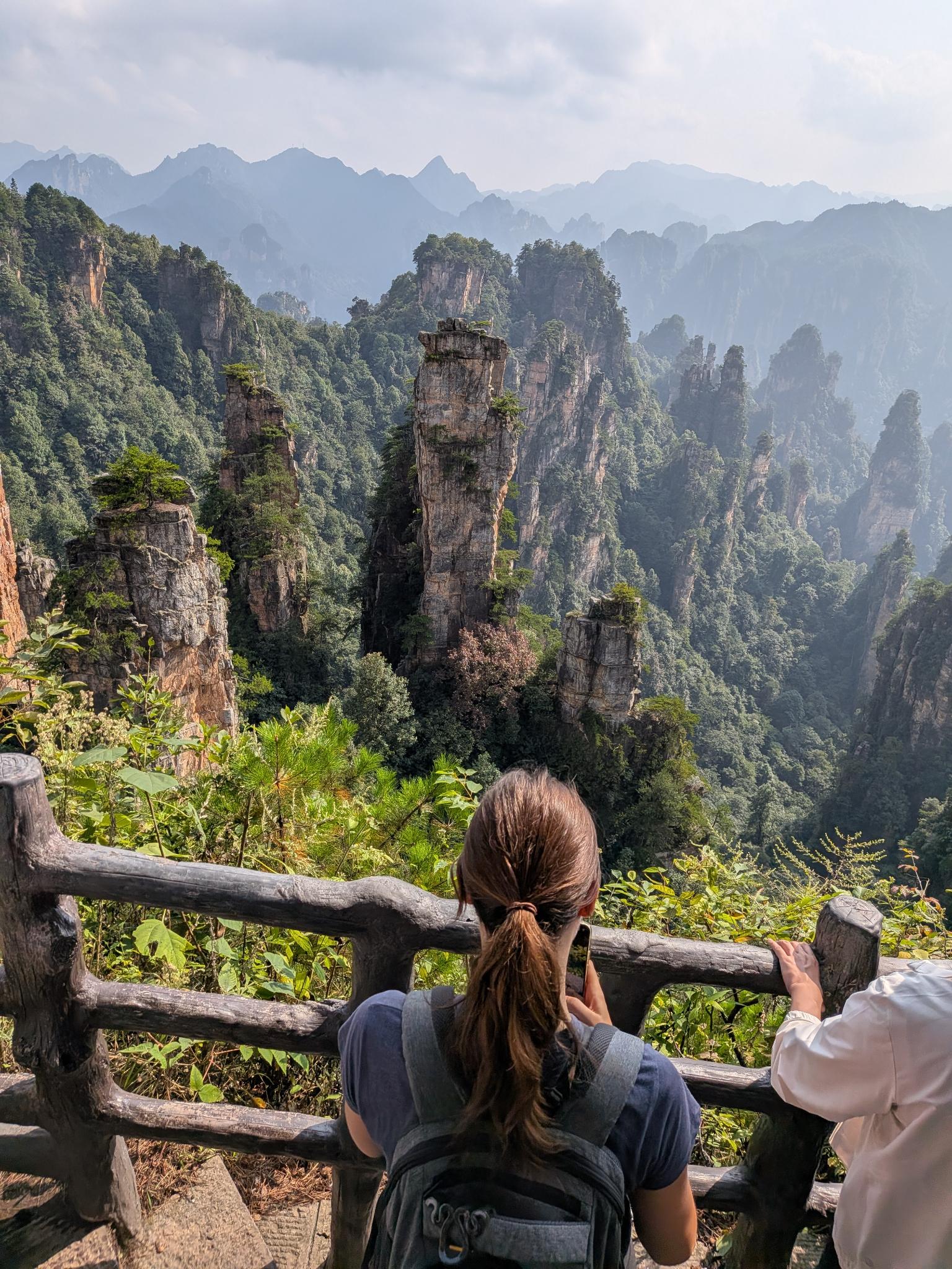 Marion qui accroche sa photo du paysage, le garde-fou en bois au premier plan