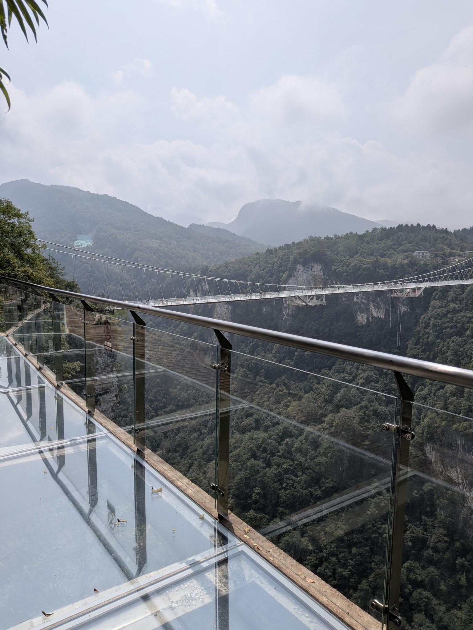 La passerelle vitrée vue depuis la plateforme, les montagnes voilées de nuages derrière