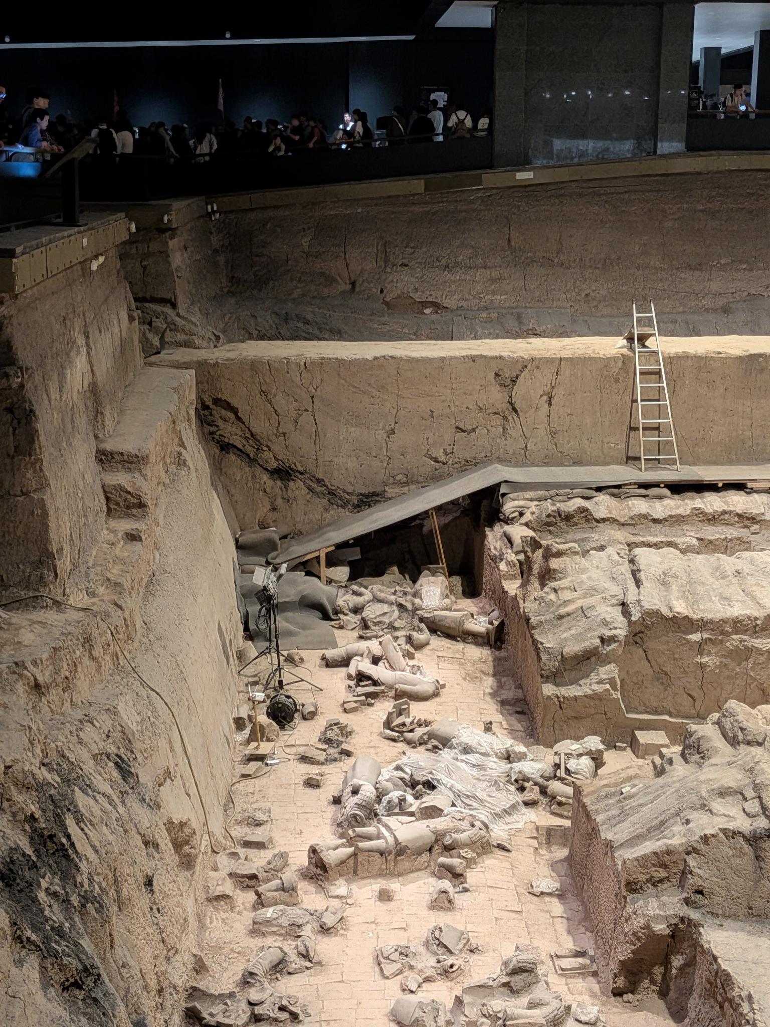 Tranchée profonde avec échelle métallique, abri de tissu, fragments en plastique, passerelle de touristes en haut
