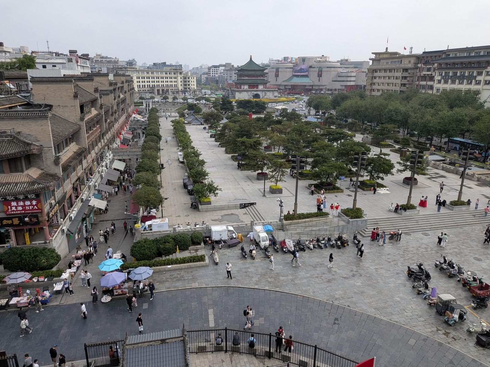 Vue sur la place de la Cloche : toits en tuiles, enseigne 鼓法推拿 足浴 SPA, hôtel ATOUR, étals sous les ombrelles bleues