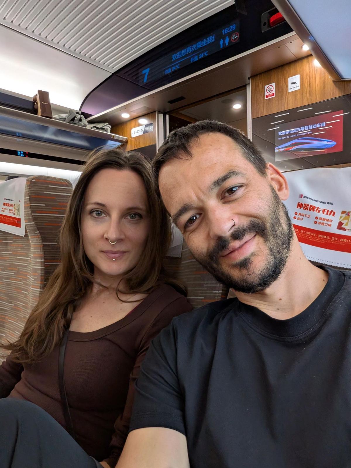 Selfie du couple dans le wagon du train, affichage voiture 7 et 16:29, panneau 欢迎乘坐复兴号智能动车组 WELCOME TO FUXING INTELLIGENT EMU