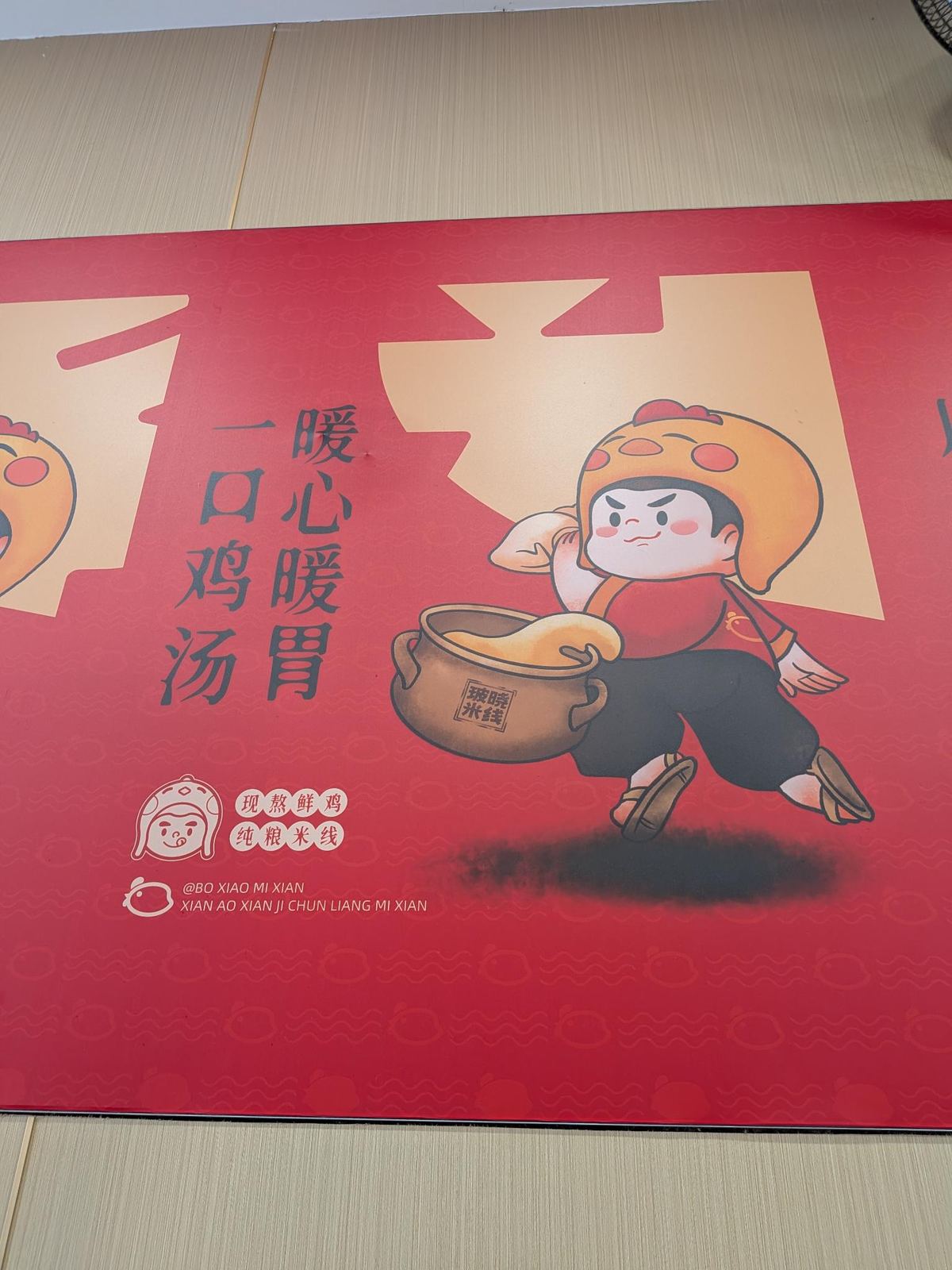 Affiche rouge du resto 玻晓米线, mascotte en dessin tenant marmites et poulet, texte 暖心暖胃 一口鸡汤 et badges 现熬鲜鸡 / 纯粮米线